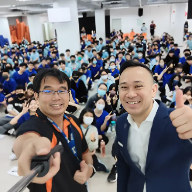 Two adults taking a selfie with a large group of secondary students in the school hall